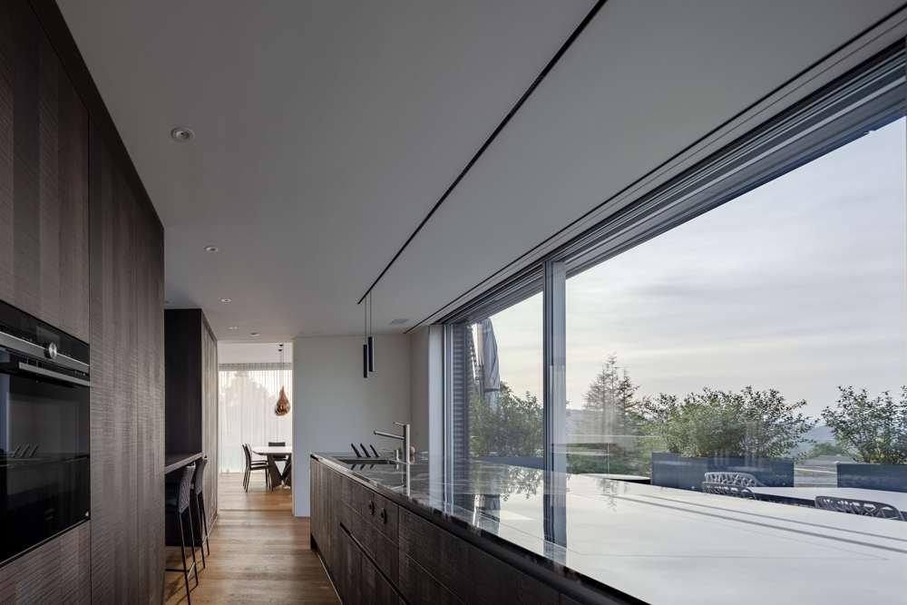 Küche im Penthouse: das rahmenlose Schiebefenster über die ganze Länge der Arbeitsfläche, die Brüstung aus Glas, dahinter Terrasse und Dachgarten.