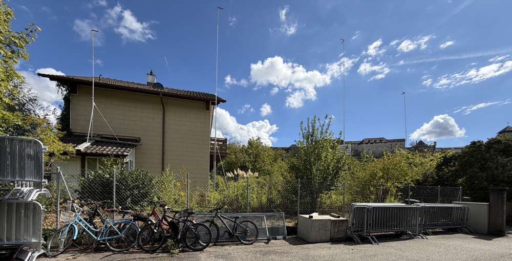 Die Parzelle an der Turnhallestrasse, September 2026: das Einfamilienhaus mit Schopf vor dem Rückbau, die Bauprofile des Neubaus gesteckt; im Hintergrund die Festung Aarburg.