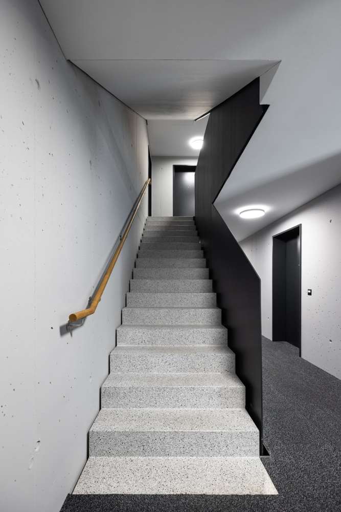 Treppenhaus: Sichtbetonwände, Treppenstufen in Terrazzo, Geländer aus schwarzem Stahlblech und Handlauf in Eiche.