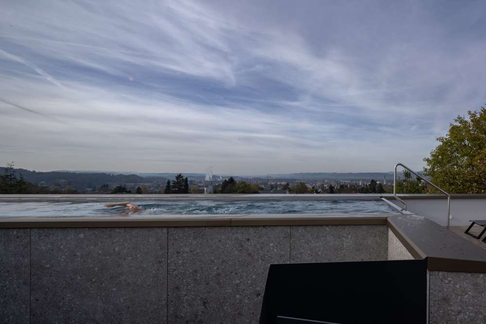 Pool im Dach: das Chromstahlbecken zwischen Patio und Terrasse, die Beckenwand mit Feinsteinzeug bekleidet, dahinter die Stadt Frauenfeld.